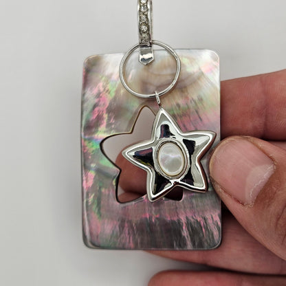 Star-shaped keychain with a pearl-like center on a metallic surface, held by a hand.
