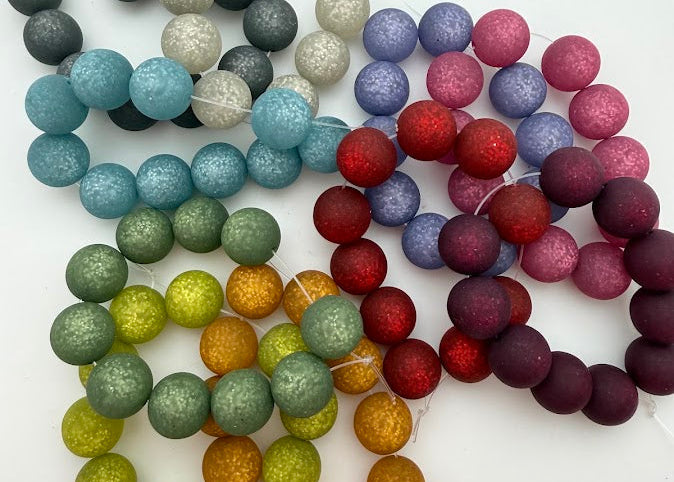 A set of multicolor round beads with a textured, glittery finish, arranged in overlapping curved rows on a plain white background. The beads come in shades of gray, blue, green, orange, red, purple, and pink.
